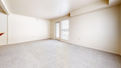 A spacious living room with a carpeted floor and a door leading to a patio at The Highlands Apartments, Elkhart, Indiana