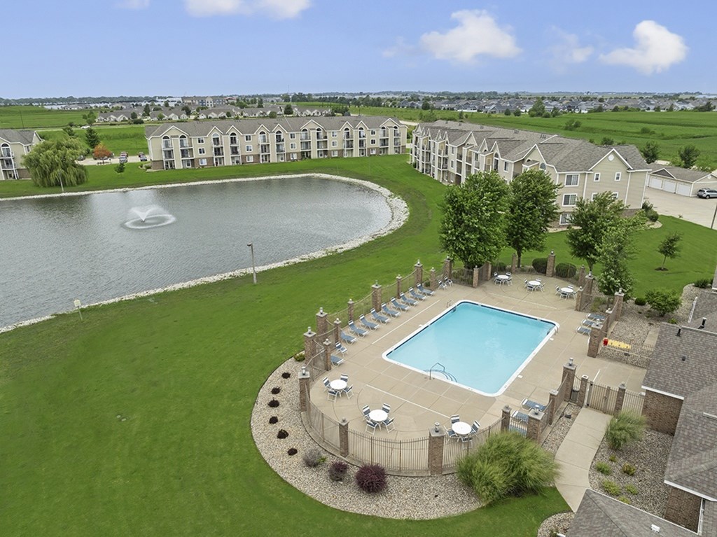 A large swimming pool surrounded by a grassy area and a pond at Hunters Pond Apartment Homes, Illinois