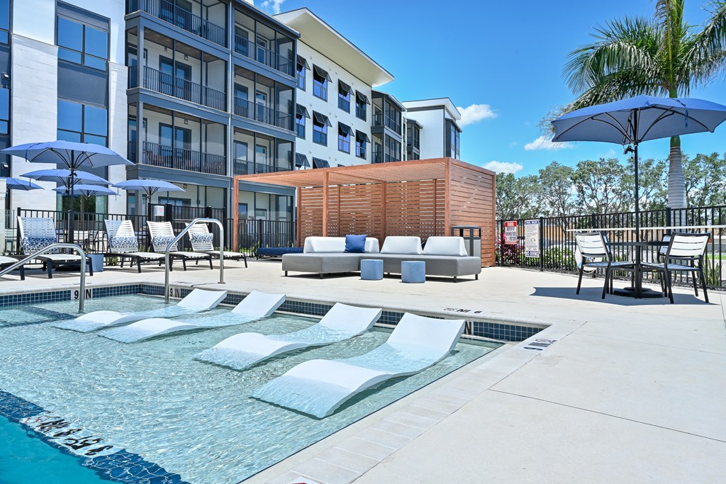 a pool with lounge chairs and umbrellas in front of an apartment building at Ironwood Flats, Florida, 33511
