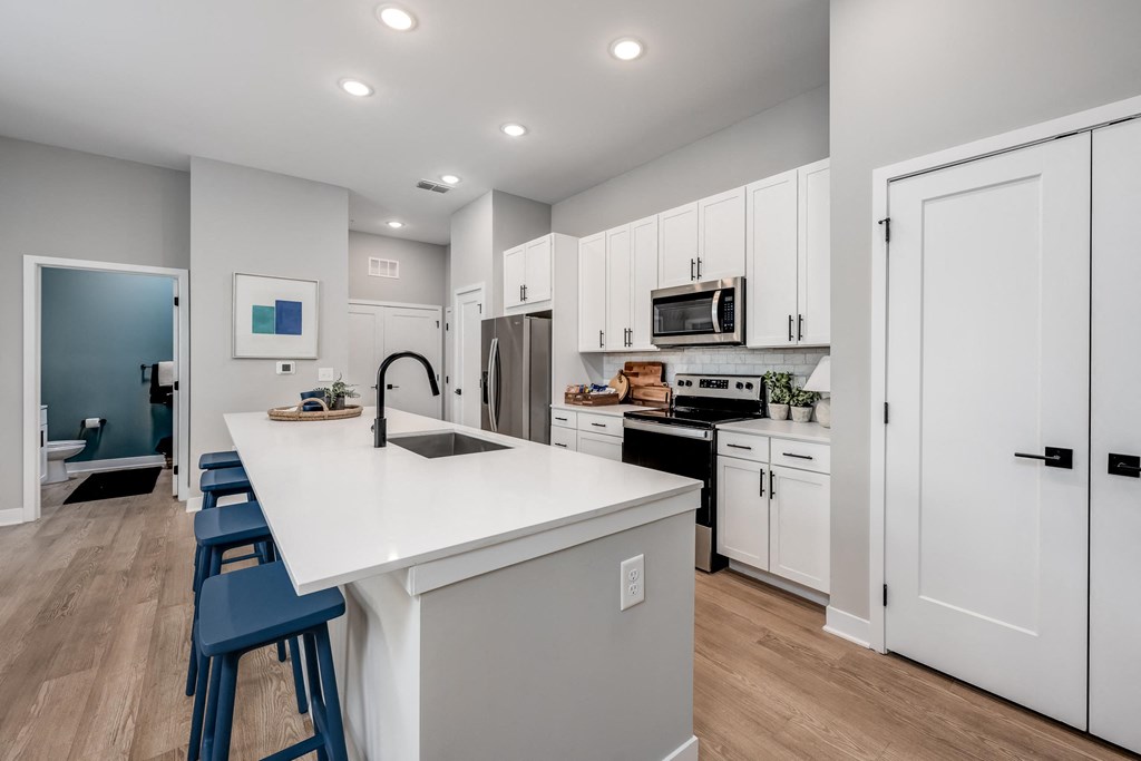a kitchen with white cabinetry and a large white island with a sink and three stools at Ironwood Flats, Brandon, Florida