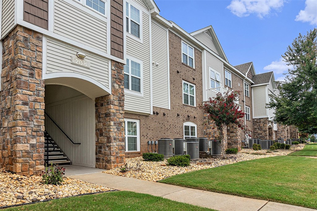 An exterior apartment building with landscaping in front and a clear blue sky above at Limestone Creek Apartment Homes, Madison, AL