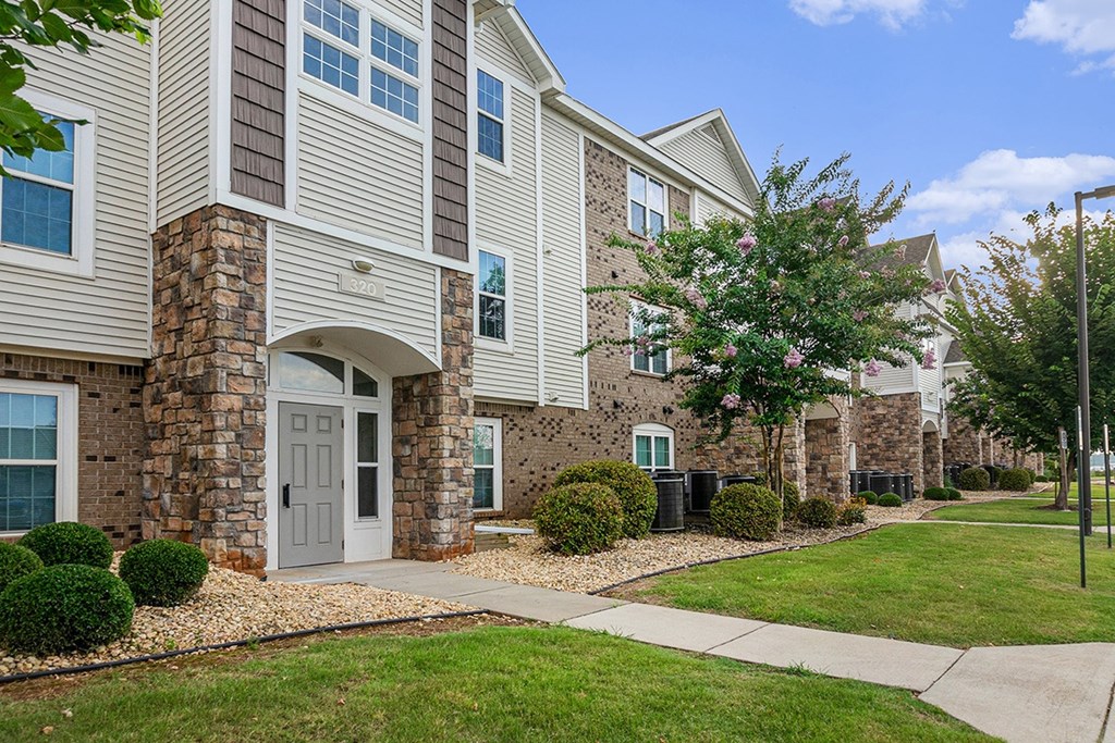 An exterior apartment building with a white door and windows with bushes in front at Limestone Creek Apartment Homes, Madison, AL