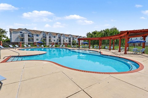 A large outdoor swimming pool surrounded by a red pergola and apartment buildings.
