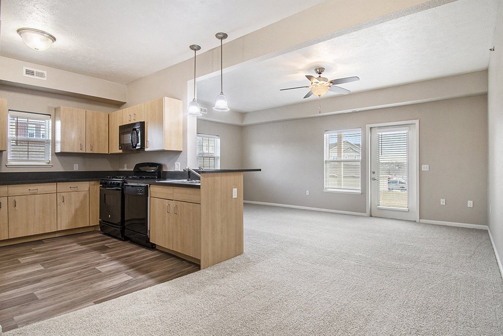 A kitchen with wooden cabinets and an enlarged living room at Lynbrook Apartments and Townhomes, Elkhorn, NE, 68022
