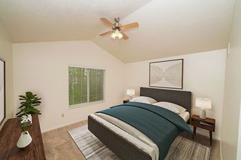 A bedroom with a bed, nightstand, and a cathedral ceiling with ceiling fan in townhome master bedroom at Lynbrook Apartments and Townhomes in Elkhorn, NE