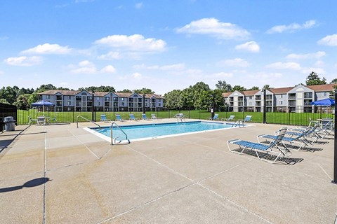 A swimming pool surrounded by chairs and apartment buildings in the background.