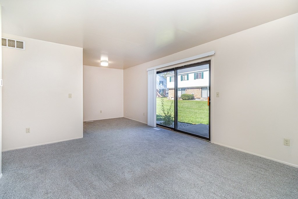 A large living room with a sliding glass door leading to a green outdoor area at Mount Royal Townhomes, Michigan