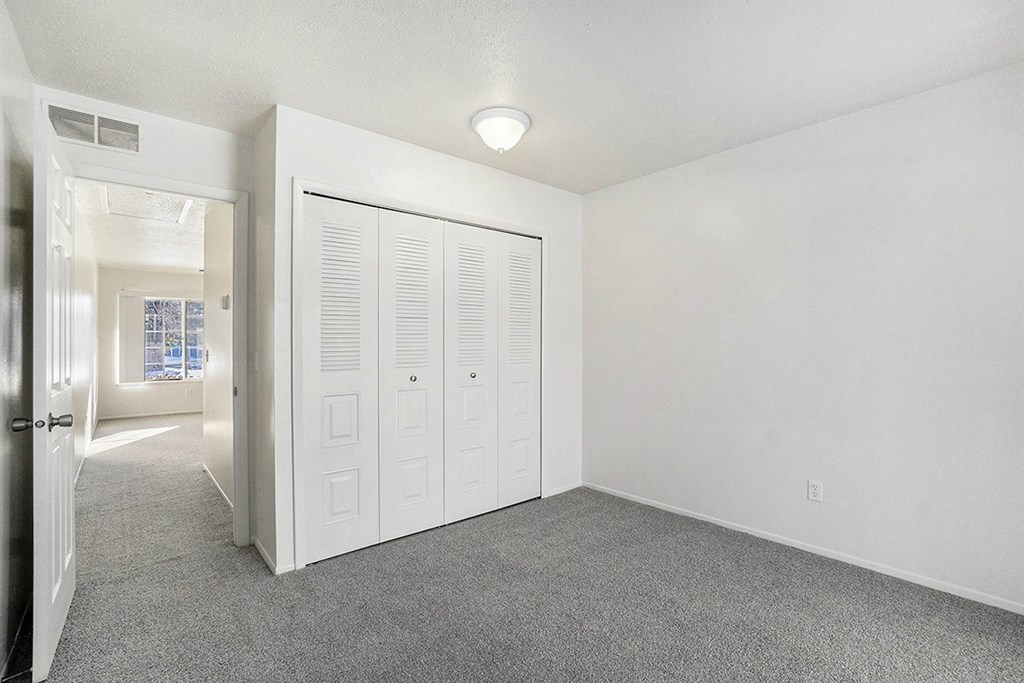 A bedroom with a grey carpet and a closet at Newport Village Apartments, Portage, MI