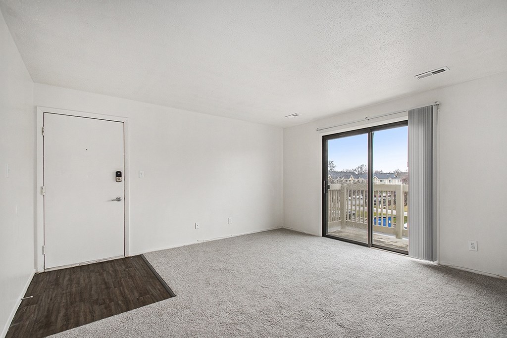 A living room with plush carpet and a slider to a private balcony with a view at Normandy Village Apartments, Michigan City, 46360