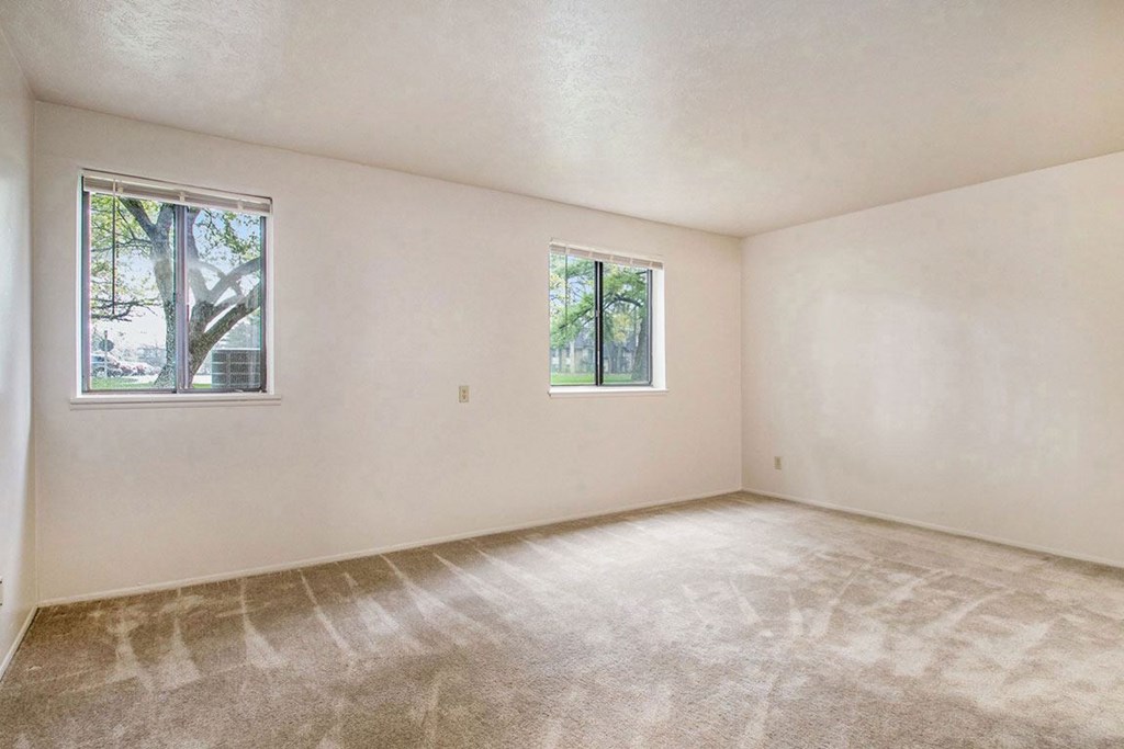 A garden style living room with two windows and carpeted floor at Normandy Village Apartments, Michigan City