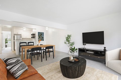 A living room with a brown couch, a wooden coffee table, and a flat screen TV mounted on the wall at Oak Shores Apartments in Oak Creek, WI