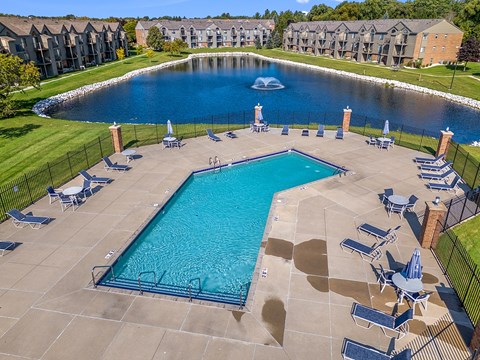 A large swimming pool surrounded by lounge chairs and a pond with a fountain behind it at Oak Shores Apartments, Wisconsin