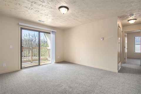 A living room with a carpeted floor and a sliding glass door leading to a balcony at Old Farm Apartments, Elkhart, Indiana