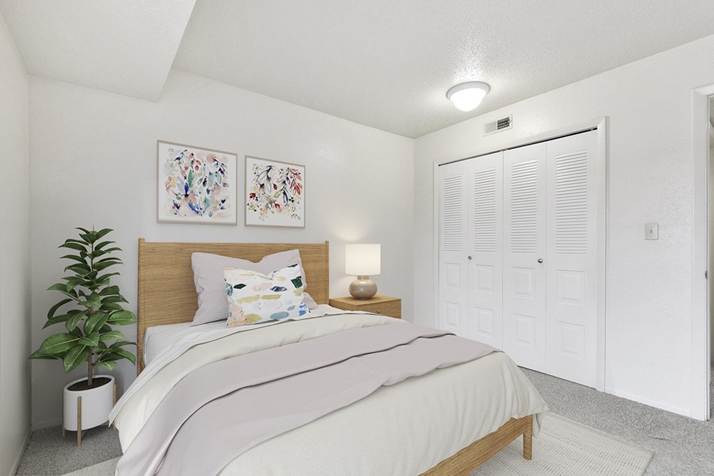 A bedroom with a bed, pictures on the wall, a potted plant, and a closet door at Old Monterey Apartments in Springfield, MO