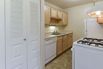 A kitchen with a white dishwasher and wooden cabinets at Old Monterey Apartments, Springfield, MO