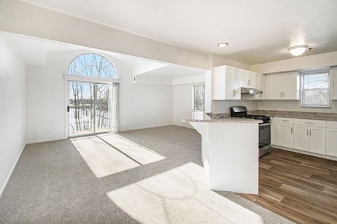 A sunny day in a spacious, empty living room with a kitchen area.