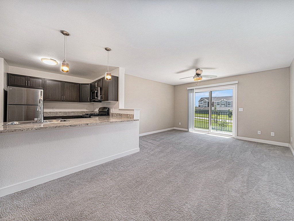 A spacious living room with a kitchen area and sliding glass doors leading to a balcony