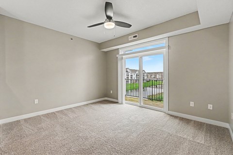 A room with a ceiling fan and a sliding glass door leading to a balcony.