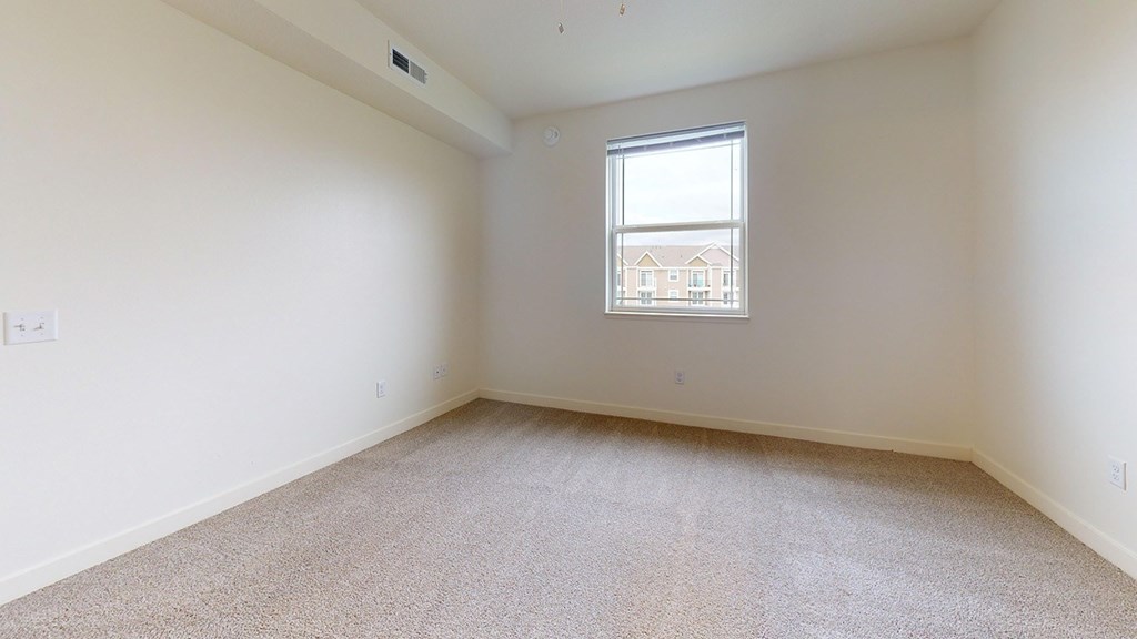 Empty bedroom with carpeted floor and a window at The Reserve at Destination Pointe apartments, Grimes, IA
