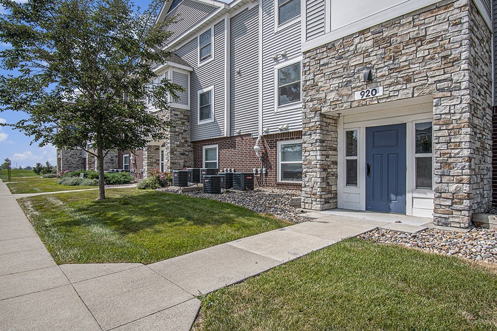 An apartment building with stone and a tree in front at The Reserve at Destination Pointe, Grimes, Iowa