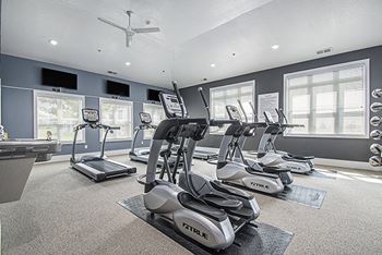 A gym with treadmills, elliptical machines, and a fan at The Reserve at Destination Pointe apartments, Grimes, IA 50111