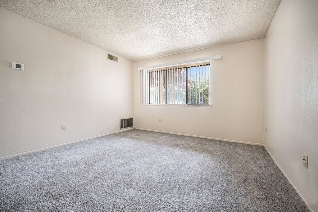 A garden style living room with a carpeted floor and a window with blinds at Seville Apartments, Michigan