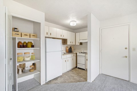 A kitchen with white appliances and cabinets with a pantry door open.