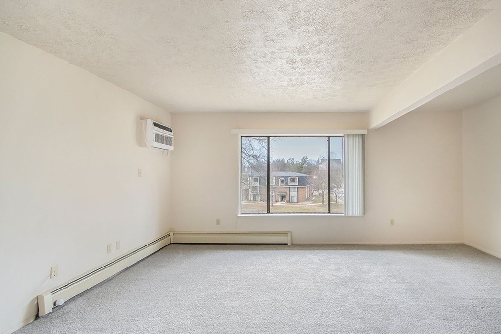 A sparsely furnished room with a window overlooking a residential area