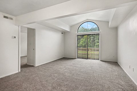 A room with a carpeted floor and a large window with a view of a fence and trees.