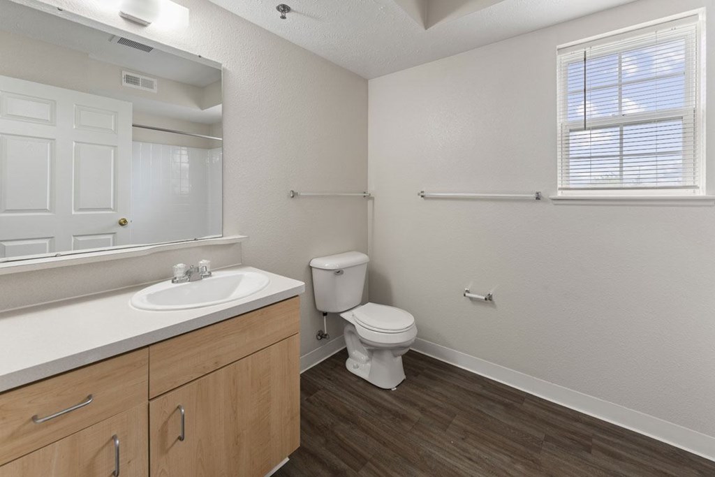 A bathroom with a window, toilet, sink, and mirror at Stoney Pointe Apartment Homes, Kansas