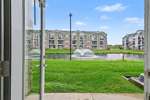 A view of a grassy area with a fountain and apartment buildings in the background.