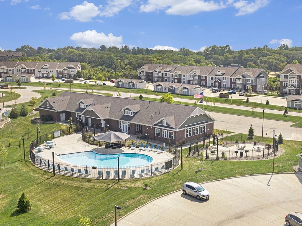 A large leasing office and community building with a pool in the middle of a grassy area at Strathmore Apartment Homes, West Des Moines, IA