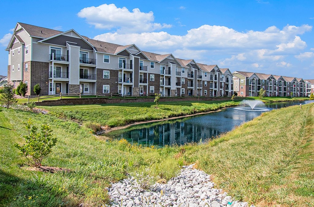 A row of apartments next to a pond with a fountain at Strathmore Apartment Homes, West Des Moines, IA