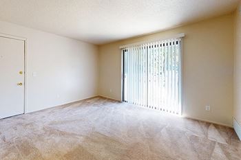A carpeted living room leading to a private patio at Swiss Valley Apartments in Wyoming, MI