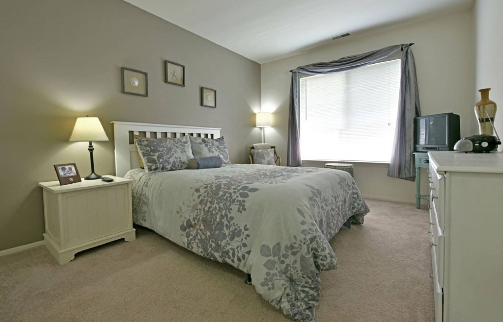 a bedroom with a bed and a dresser in front of a window at Sycamore Creek Apartments, Lake Orion, Michigan