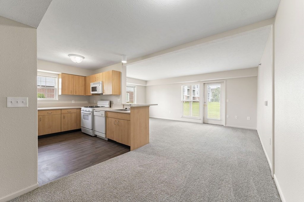 A spacious kitchen and enlarged living room leading to a patio at Tall Oaks Apartment Homes, Michigan, 49009