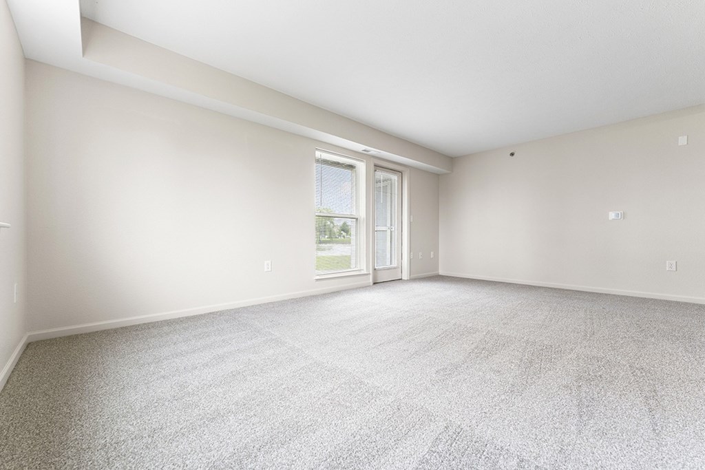 A spacious living room with a carpeted floor and a french door leading outside at Tall Oaks Apartment Homes, Michigan, 49009