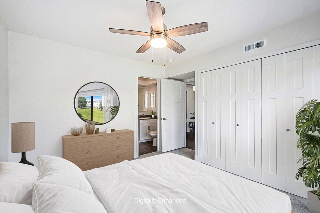 a bedroom with a bed and a ceiling fan leading to a bathroom at The Crossings Apartments, Michigan, 49508
