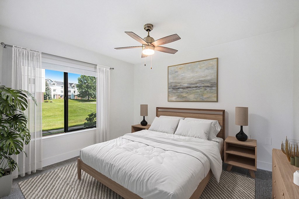 A bedroom with a large bed, a ceiling fan, and a large window at Byron Lakes Apartments, Michigan, 49315