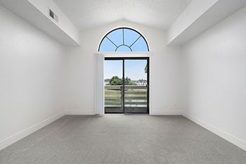 A living room with a large arched window and cathedral ceiling with a view at The Crossings Apartments, Grand Rapids, Michigan