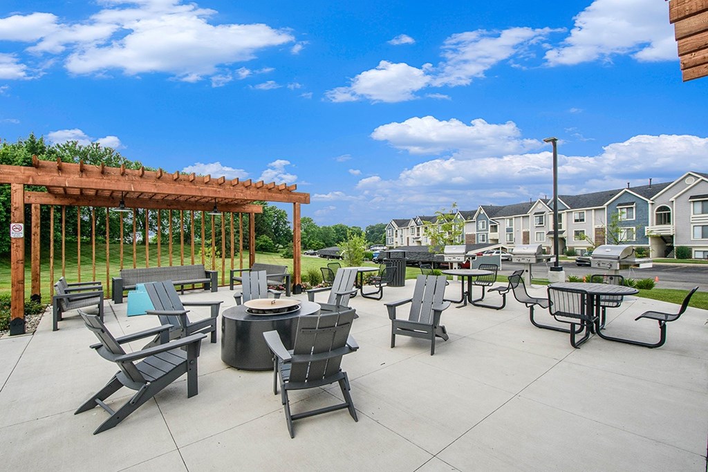 an outdoor pergola with tables and fire pit with seating at The Crossings Apartments, Michigan, 49508
