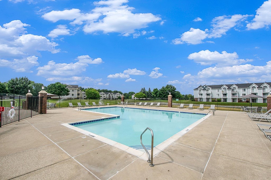 A large swimming pool surrounded by a concrete patio and lounge chairs at The Crossings Apartments, Michigan