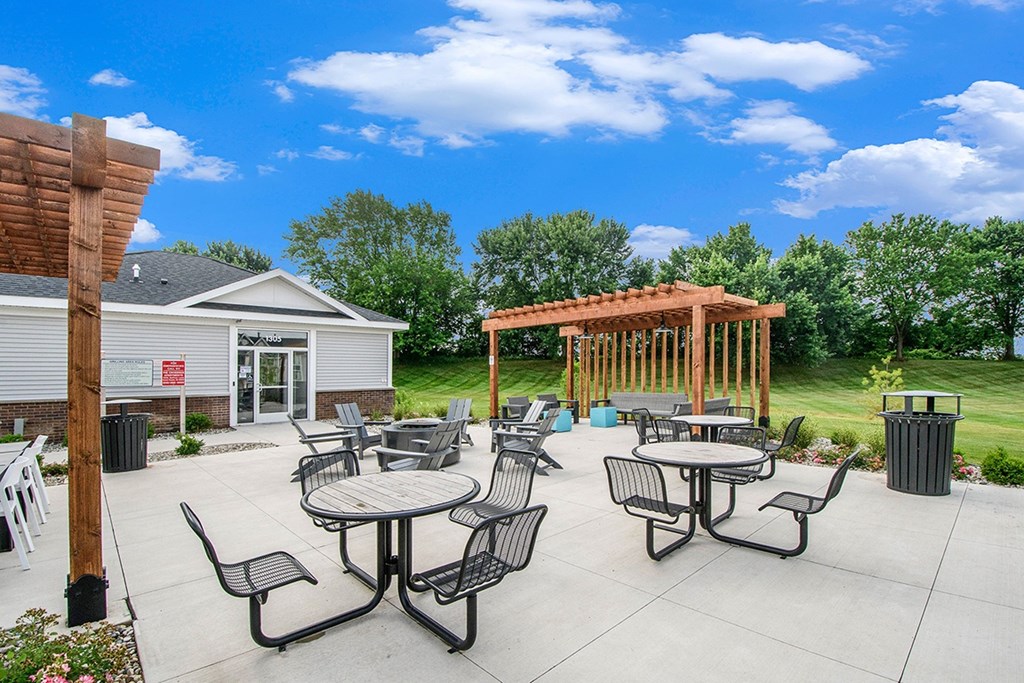 an outdoor patio with pergolas, a fire pit, tables and chairs at The Crossings Apartments, Michigan, 49508