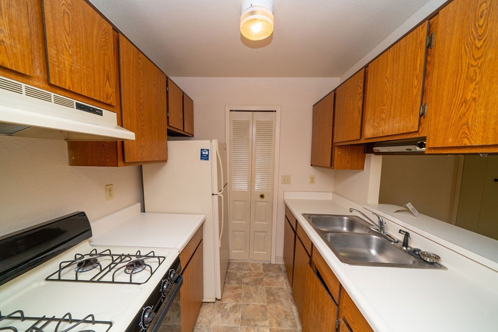 A kitchen with a gas stove and wooden cabinets at Trappers Cove Apartments, Lansing