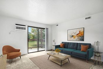 A living room with a couch, a chair, a coffee table, and a slider to a private balcony at Trappers Cove Apartments in Lansing, MI