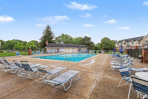A pool surrounded by chairs and trees.