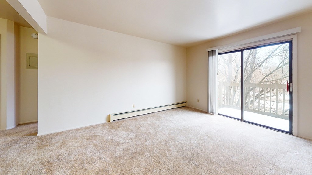 A living room with a carpeted floor and a sliding glass door to a balcony at Waverly Park Apartments, Lansing