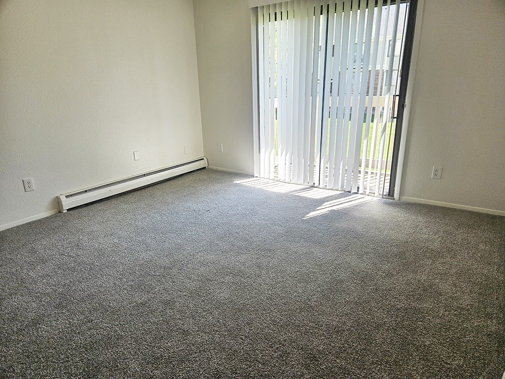 A room with a carpeted floor and a window with blinds.