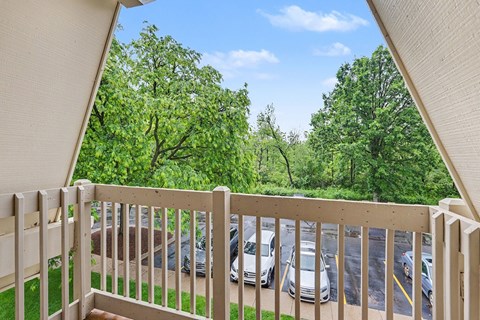 A balcony with a view of a parking lot and trees at Waverly Park Apartments, Lansing