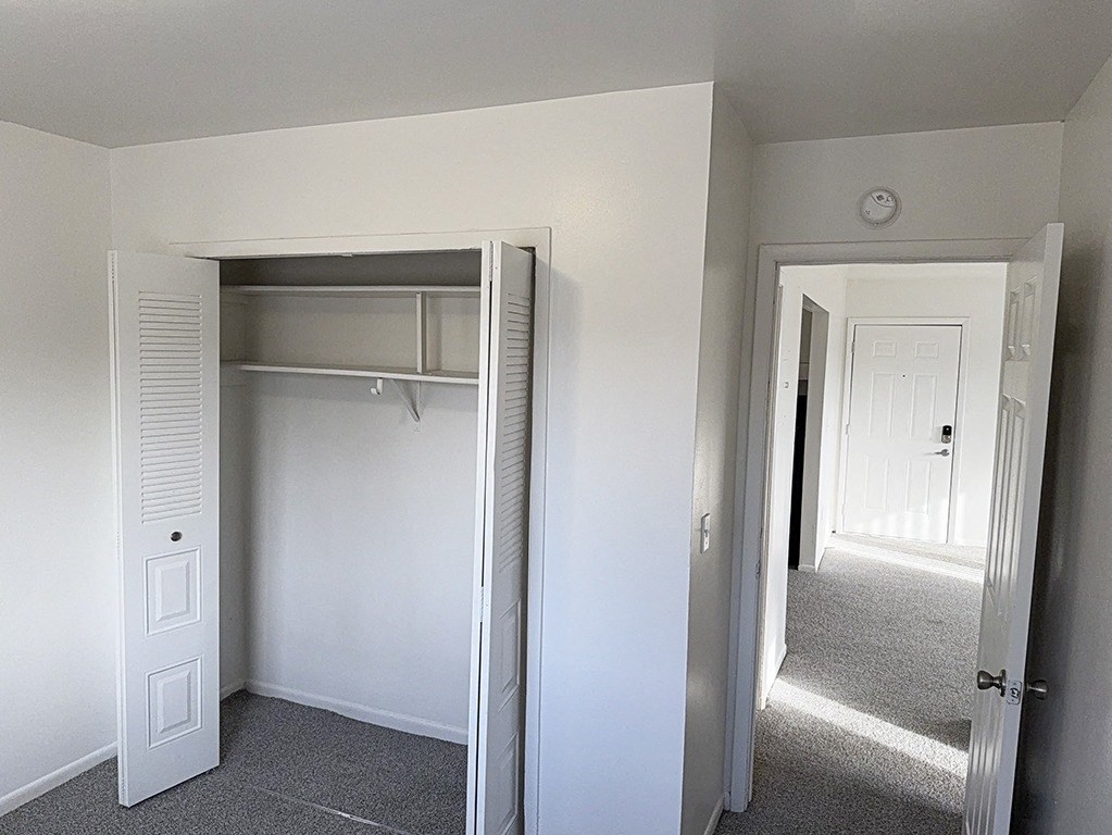 A bedroom with a white closet with a door open to a hallway at Waverly Park Apartments, Lansing